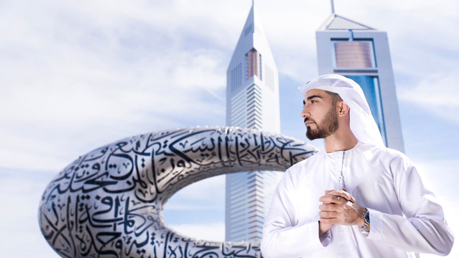 A man in traditional Emirati dress before the Museum of the Future and Emirates Towers